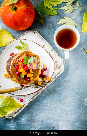 Herbstliches frühstück Idee, Kürbis Pfannkuchen, mit Scheiben von Kürbis, Ahornsirup oder Honig, Moosbeere, auf einem blauen konkreten Hintergrund, Platz für Text Stockfoto