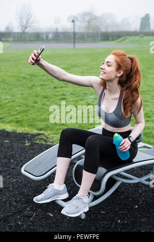 Lächelnde junge Frau mit langen roten Haaren Sportkleidung tragen, beim Sport im Freien. Stockfoto