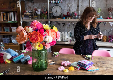 Frau, die in einer Werkstatt, Bündel von farbenfrohen handgefertigten Stoff Blumen in einer Vase auf dem Tisch. Stockfoto