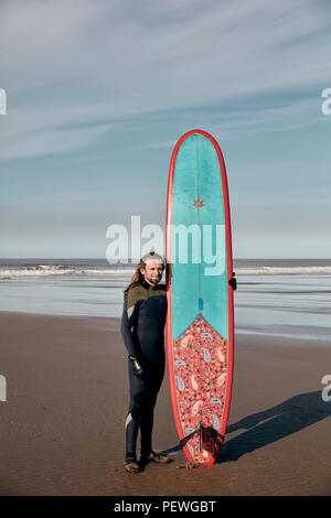 Porträt eines Mannes mit einer dekorierten Surf Board an einem Sandstrand Stockfoto