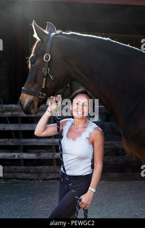 Lächelnde Frau stehen im Freien bei stabilen, braunes Pferd von rein. Stockfoto