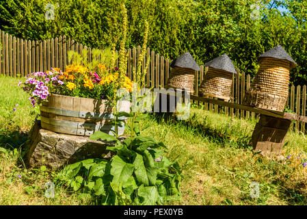 Drei kleine Bienenstöcke und ein Blumentopf mit bunten Blumen. Der Garten ist hügelig, so dass der Bienenstöcke und der Blumentopf lehnt sich ein wenig. Sommer in der Garde Stockfoto