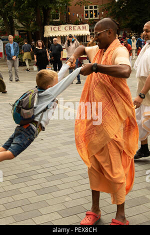 Männliches Hare Krishna-Mitglied schwingt jungen Jungen in Kings Square, York, North Yorkshire, England, Großbritannien. Stockfoto