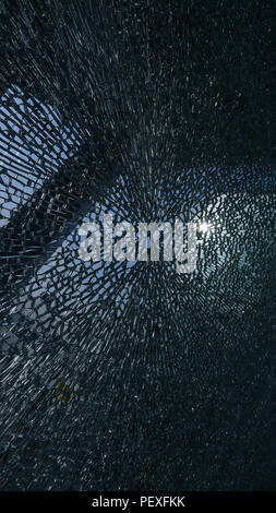 Risse in der Oberfläche des Glases mit einem kleinen Loch in der Mitte Stockfoto