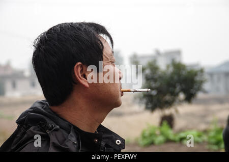 Eine Nahaufnahme von der Seite ein rauchender junger chinesischer Mann Gesicht Stockfoto