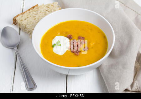 Butternut und Speck Suppe mit saurer Sahne, Speck und Schalotten Aufstockung in weiße Schüssel auf weißem rustikalen Tisch mit Brot Stockfoto
