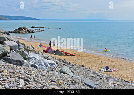 Urlauber genießen das Paddeln im warmen Sommer Meer und Spielen am Strand von Wisemans Brücke, einem kleinen Dorf an der Küste in der Nähe von Tenby in West Wales. Stockfoto