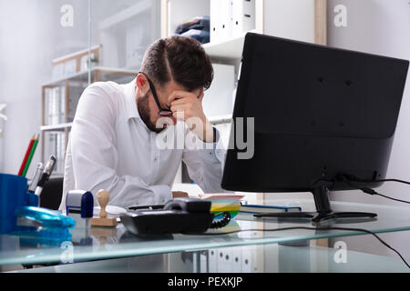 Müde junge Unternehmer Sitzen im Büro mit Computer auf dem Schreibtisch Stockfoto
