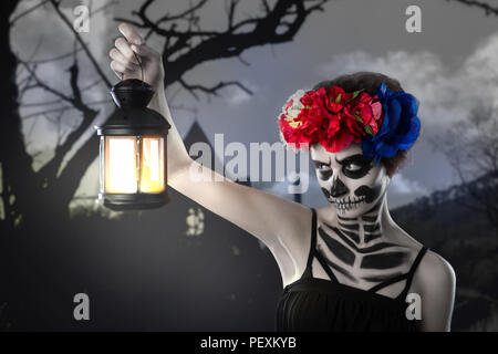 Halloween Hexe. Schöne Frau Tragen santa muerte Maske casting Zauber in der Nähe der Glühbirne vor dem Hintergrund einer unheimlichen Wald Stockfoto