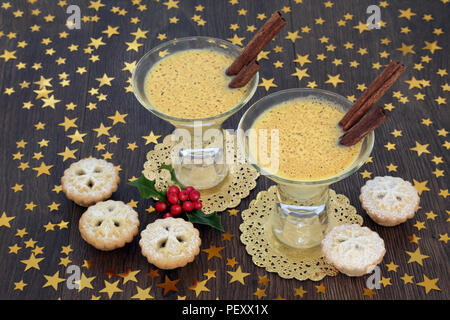 Weihnachten Eierlikör trinken mit traditionellen Mince Pies, Gold Star Dekorationen und Winter Stechpalme Beeren auf Eiche rustikal Hintergrund. Festliche Thema. Stockfoto