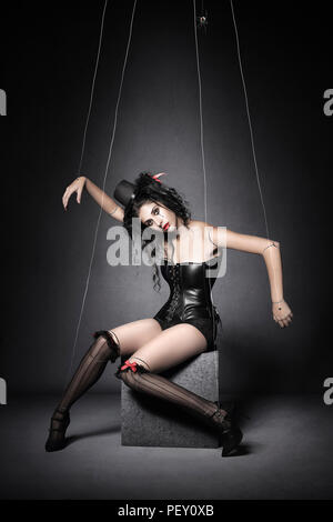 Frau posiert als Marionette Marionette in Schwarz und Rot mit transparenten Zeichenfolgen. Konzeptionelle Kunst über Manipulation und Kontrolle. Stockfoto