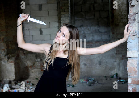 Frau in den Ruinen, die Messer in der Hand. Weibliche Modell mit schwarzen Kleid in Ruinen, alten Palast in Polen. Stockfoto