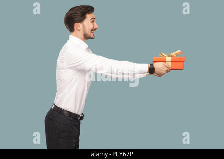 Profil Seitenansicht lachendes Smiley bärtiger Mann im weißen Hemd und mit roten Geschenkkarton, geben und Seite mit toothy Lächeln. Hallenbad, Stu Stockfoto