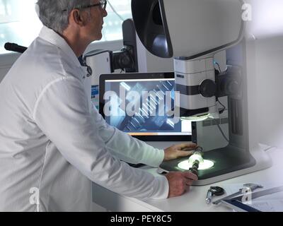 Ingenieur mit einem Stereo Mikroskop eine hergestellte Komponente im Prozess der Qualitätskontrolle zu überprüfen. Stockfoto