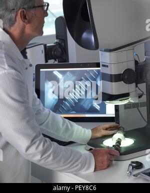 Ingenieur mit einem Stereo Mikroskop eine hergestellte Komponente im Prozess der Qualitätskontrolle zu überprüfen. Stockfoto