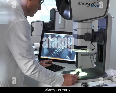 Ingenieur mit einem Stereo Mikroskop eine hergestellte Komponente im Prozess der Qualitätskontrolle zu überprüfen. Stockfoto