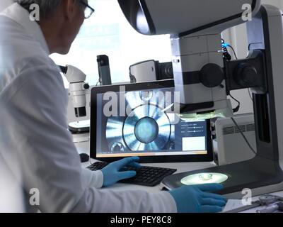 Ingenieur mit einem Stereo Mikroskop eine hergestellte Komponente im Prozess der Qualitätskontrolle zu überprüfen. Stockfoto