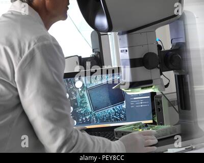 Ingenieur mit einem Stereo Mikroskop eine Leiterplatte während der Prozess der Qualitätskontrolle zu überprüfen. Stockfoto