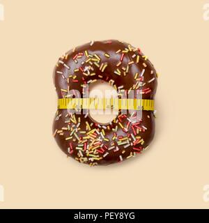 Das Nähren, konzeptionelle Bild. Schokolade Donut mit Zucker Litzen und Maßband, Studio gedreht. Stockfoto