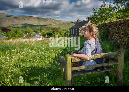 Eine attraktive Frau mittleren Alters saß auf einer Bank in der Sonne mit Blick auf Wasdale, Cumbria, Lake District National Park. Stockfoto