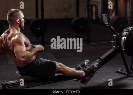 Volle Länge Seitenansicht erschossen. Ein junger Mann aus der Arbeit mit einem Indoor Rower. Lifestyle und Hobby Konzept Stockfoto