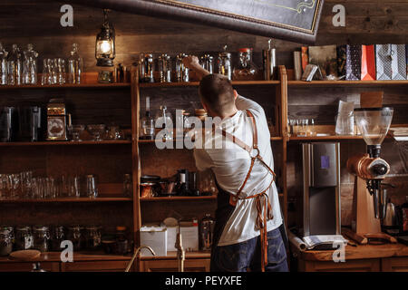 Eine junge Barista ist die Gläser auf dem Regal im Kaffee Zimmer Stockfoto