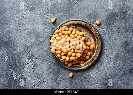 Würzige beschichtet gebratene Erdnüsse auf grauem Hintergrund. Blick von oben auf die Snacks und die Muttern. Stockfoto