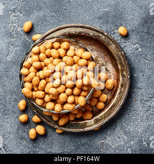 Würzige beschichtet gebratene Erdnüsse auf grauem Hintergrund. Blick von oben auf die Snacks und die Muttern. Stockfoto