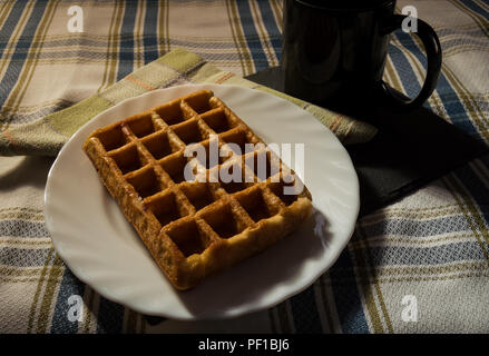 Frühstück: süße Waffeln, schwarz Tasse Kaffee und Serviette. Essen und Trinken auf blackboard Fach und karierte Tischdecke. Stockfoto