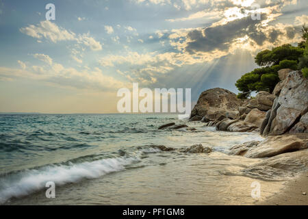 Sonnenstrahlen durch die Wolken über erstaunliche Koviou Strand und schöne rock Struktur mit einer Kiefer auf der Oberseite Stockfoto