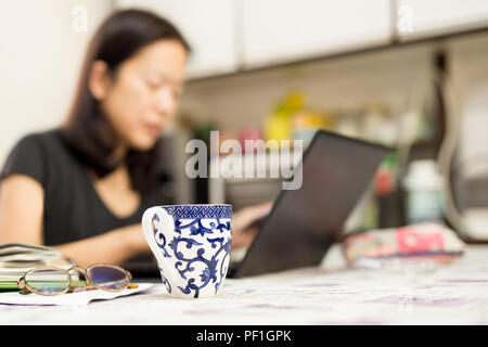 Ausgewählte Schwerpunkte der Kaffeetasse Frau mit Computer zu Hause arbeiten Stockfoto