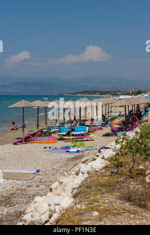 Liegestühle, Sonnenliegen und Rattan oder Korbweide tropische Sonnenschirme und Regenschirme an einem Sandstrand auf der griechischen Insel Korfu in Griechenland. Stockfoto
