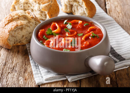 Geschmorte Tintenfische in Tomatensauce mit Gewürzen, Zwiebeln, Pfeffer und Petersilie close-up in eine Schüssel und frisches Brot mit Oliven auf den Tisch. Horizontale Stockfoto