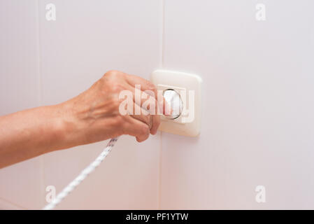 Senior hand Plug elektrische Kabel in Weiß Steckdose Stockfoto