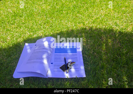 Papiere mit Lektionen zu studieren, Bleistift und Schlüssel im Schatten auf dem Rasen Stockfoto