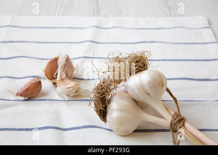 Knoblauchzehen, Knoblauch Zwiebeln auf Tuch über weiße Holzfläche, Seitenansicht. Stockfoto