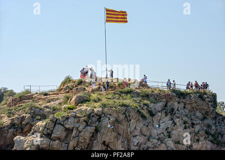 Touristen sind in der Nähe der Senyera Flagge am Mast auf Sa Palomera Rock in Blanes, Costa Brava, Katalonien, Spanien. Stockfoto