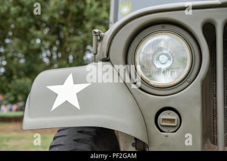 Nahaufnahme, flacher Fokus auf einen vollständig restaurierten, ikonischen US Army Jeep aus dem 2. Weltkrieg, der einen Scheinwerfer, einen weißen Stern und einen Kühler zeigt. Stockfoto