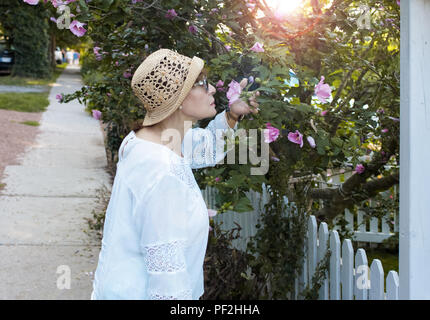 Reife Frau Spaziergänge, stoppt, und Gerüche einige Blumen von einem Baum. Stockfoto