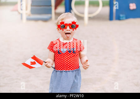 Portrait von adorable kleine süße blonde kaukasische Baby Kleinkind Mädchen, dass kanadische Flagge. Weibliches Kind tragen lustig Ahornblätter Sonnenbrille celebrat Stockfoto