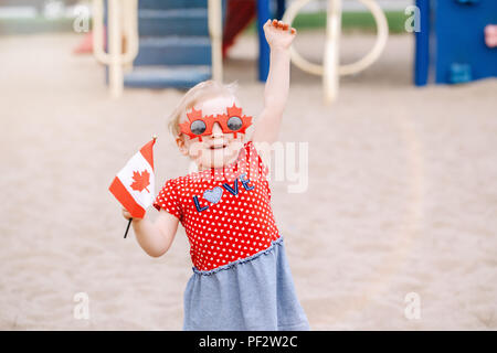 Portrait von adorable kleine süße blonde kaukasische Baby Kleinkind Mädchen, dass kanadische Flagge. Weibliches Kind tragen lustig Ahornblätter Sonnenbrille celebrat Stockfoto