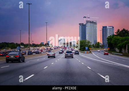 Nacht Verkehr. Autos sind auf der Autobahn Straße bei Sonnenuntergang abends in typisch geschäftigen amerikanischen Stadt. Schöne tolle Nacht urban Ansicht mit roten, gelben und blauen Himmel Stockfoto