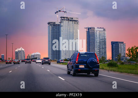 Nacht Verkehr. Autos sind auf der Autobahn Straße bei Sonnenuntergang abends in typisch geschäftigen amerikanischen Stadt. Schöne tolle Nacht urban Ansicht mit roten, gelben und blauen Himmel Stockfoto