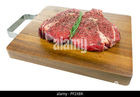 Gepfeffert raw Rib Eye Steaks mit Rosmarin auf einem hölzernen Schneidebrett in einem isolierten weißen Hintergrund Stockfoto