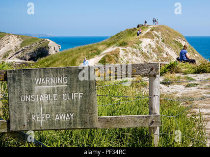 Touristen ignorieren Gefahr instabiler Cliff sign an Lulworth Cove, Dorset, Großbritannien am 11. Juli 2013 Stockfoto