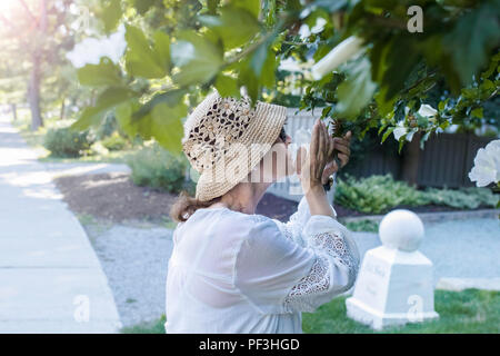 Reife Frau Spaziergänge, stoppt, und Gerüche einige Blumen von einem Baum. Stockfoto