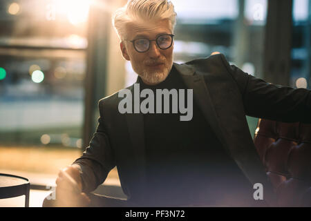 Portrait von stattlichen Reife Unternehmer Sitzen im Büro. Mann in formelle Kleidung sitzen auf Office Lobby. Stockfoto