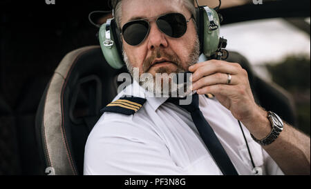 Reife männliche Hubschrauberpiloten mit Headset im privaten Hubschrauber. Nahaufnahme der männlichen Pilot im Gespräch über das Headset im Cockpit eines Hubschraubers. Stockfoto