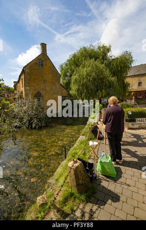 Ein Künstler Malerei durch den Fluss in Bourton auf dem Wasser. Stockfoto