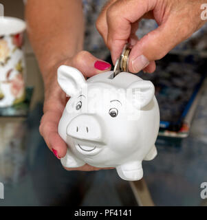 Setzen des Geldes in einem weißen piggy Bank durch womans' geführt wird. mans hand mit der Cash Stockfoto